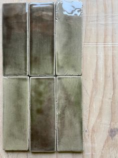 four square pieces of green glazed tile on a wooden surface