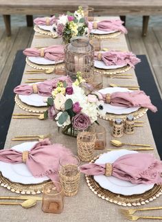 the table is set with pink napkins and gold place settings