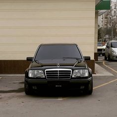 a black mercedes benz parked in a parking lot next to a building with two cars behind it