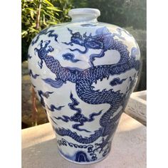 a large blue and white vase sitting on top of a stone table next to trees