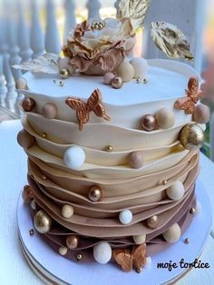 a multi layer cake decorated with gold and white frosting, butterflies and flowers on top