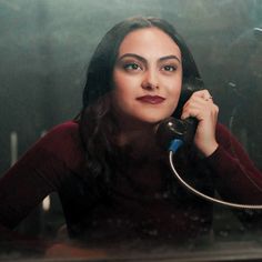 a woman sitting at a table talking on a phone while holding a cord to her ear