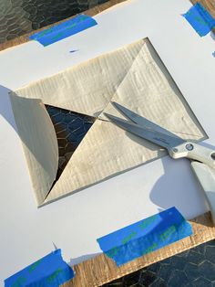 a pair of scissors cutting paper on top of a piece of cardboard with blue tape