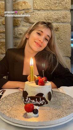 a woman sitting at a table in front of a cake with two candles on it