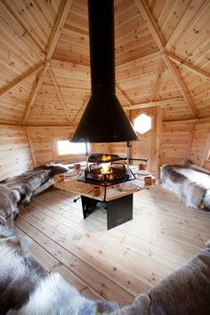 the inside of a wooden cabin with a fire place in the center and fur on the floor