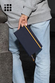 a person holding a book in their left hand while sitting on a stone bench with his legs crossed