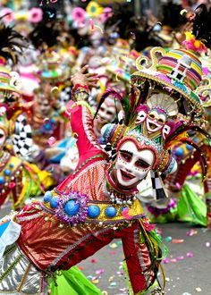 people dressed in colorful costumes and masks are dancing on the street with confetti all around them