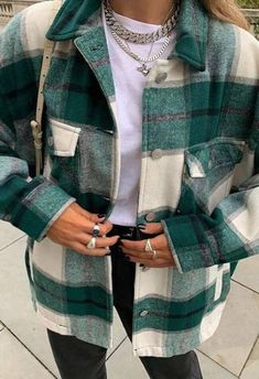 a woman with pink hair wearing a green and white plaid jacket, black pants, silver necklaces