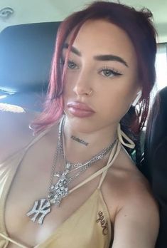 a woman with pink hair and tattoos on her chest sitting in the back seat of a car