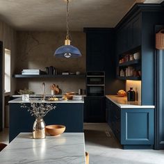 a kitchen with dark blue cabinets and marble counter tops, gold pendant lights over the island