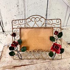 a small metal frame with red flowers and hearts on the front is sitting on a wooden table