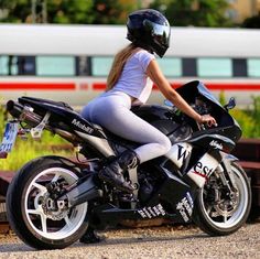 a woman riding on the back of a motorcycle next to a rail road track with a train in the background