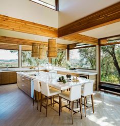 a large open kitchen and dining room area with wood paneled walls, hardwood flooring and windows