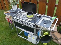 an outdoor cooking station with pots and pans on it in the grass next to a fence