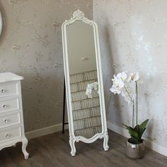 a white dresser sitting next to a tall mirror on top of a wooden floor in a room