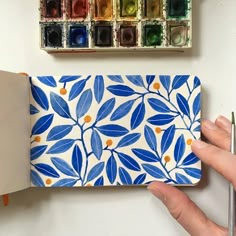 a hand holding a blue and white floral patterned notebook with watercolors on it