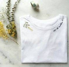 a white t - shirt sitting on top of a table next to flowers and a roll of tape