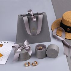 an assortment of jewelry and accessories are displayed on a gray surface with a magazine, hat, bracelets, and earring rings