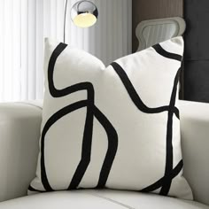 a black and white pillow sitting on top of a white couch next to a window