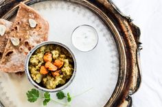 a plate with some food on it next to a small bowl of soup and pita bread