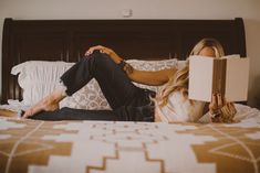 a woman laying on top of a bed holding an open book in her hand and looking at the camera