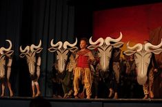 a group of men standing on top of a stage next to white bull head masks