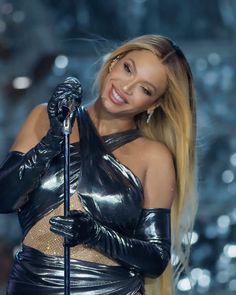 a woman with long hair and gloves on holding a microphone in front of her face