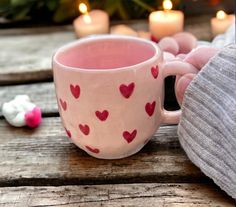 a person holding a pink coffee cup with hearts on it and candles in the background