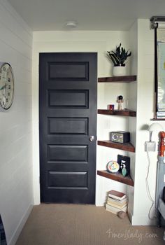 a black door in a white room next to a shelf with books and a clock