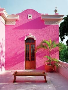 a pink building with a wooden bench in front of it and a potted plant next to the door