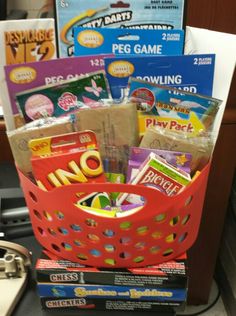 a red basket filled with lots of games and snacks on top of a counter next to a pile of books