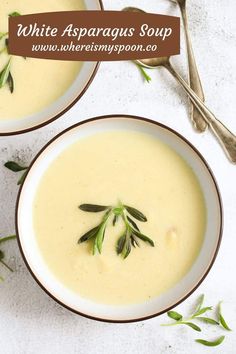 two bowls of white asparagus soup with spoons and green leaves on the side