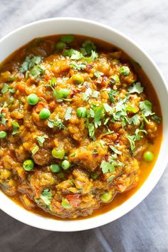 a white bowl filled with food and garnished with cilantro, green onions and peas