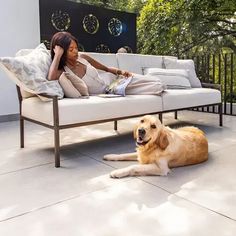 a woman sitting on a couch next to a dog laying on the ground in front of her