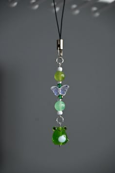 a green and white glass beaded necklace hanging from a black cord on a gray background