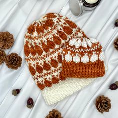 two knitted hats sitting on top of a white table next to pine cones and candles