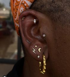 a close up of a person with ear piercings on their ears and wearing an orange bandana