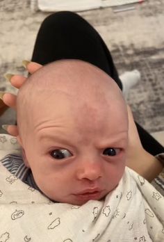 a balding baby is being held by a woman with scissors in her hair and looking at the camera