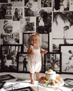 a baby standing in front of a cake with pictures on the wall behind it,