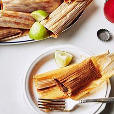 two plates with tamales and limes on them