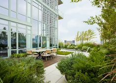 an outdoor dining area with tables and chairs surrounded by greenery in front of a large glass building