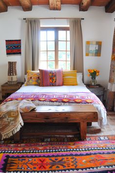 a bed with colorful pillows and blankets on top of it in a bedroom next to a window