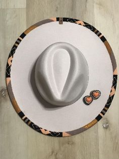 a white hat sitting on top of a wooden floor next to a pair of earrings