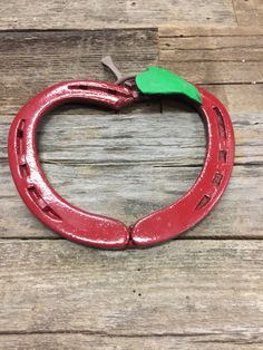 a red apple shaped like a horseshoe with a green leaf on the end, sitting on a wooden surface