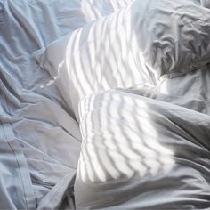 an unmade bed covered in white sheets and pillows with the sun shining on them