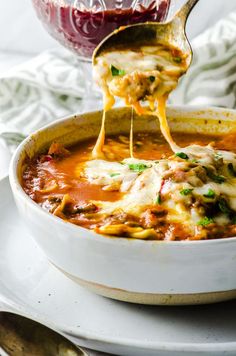 a spoon full of soup being lifted from a bowl with another dish in the background