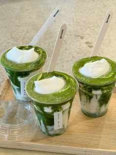 three green smoothies with whipped cream in them sitting on a wooden tray, ready to be eaten