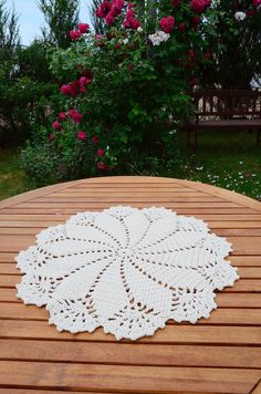 a white doily sitting on top of a wooden table in front of pink flowers