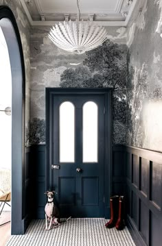 a dog sitting in front of a black door with white and gray wallpaper on it