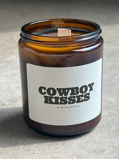 a candle with the words cowboy kisses on it sitting on a countertop next to a cup